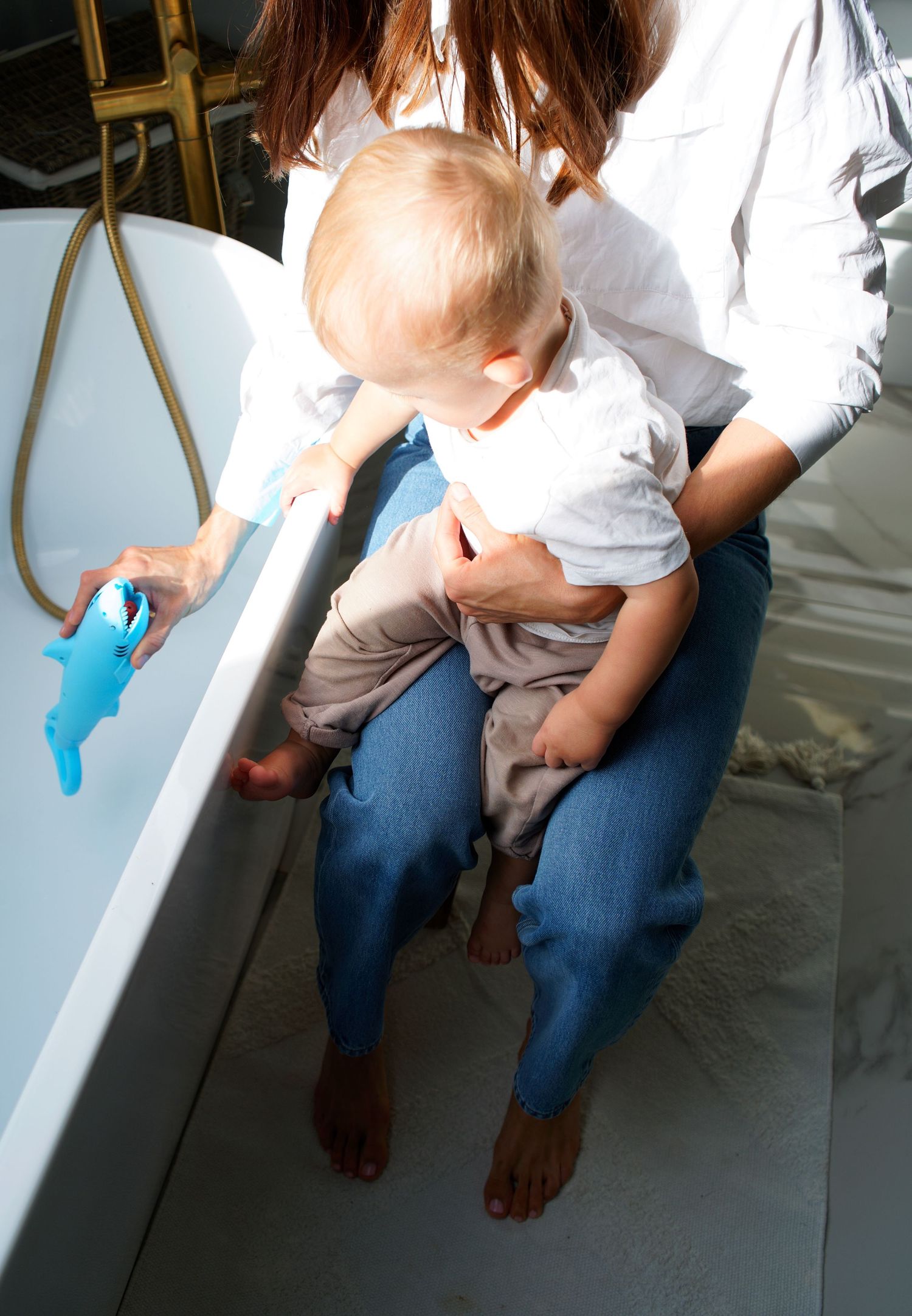 Person sitting on white surface wearing jeans with bare feet in artistic composition.