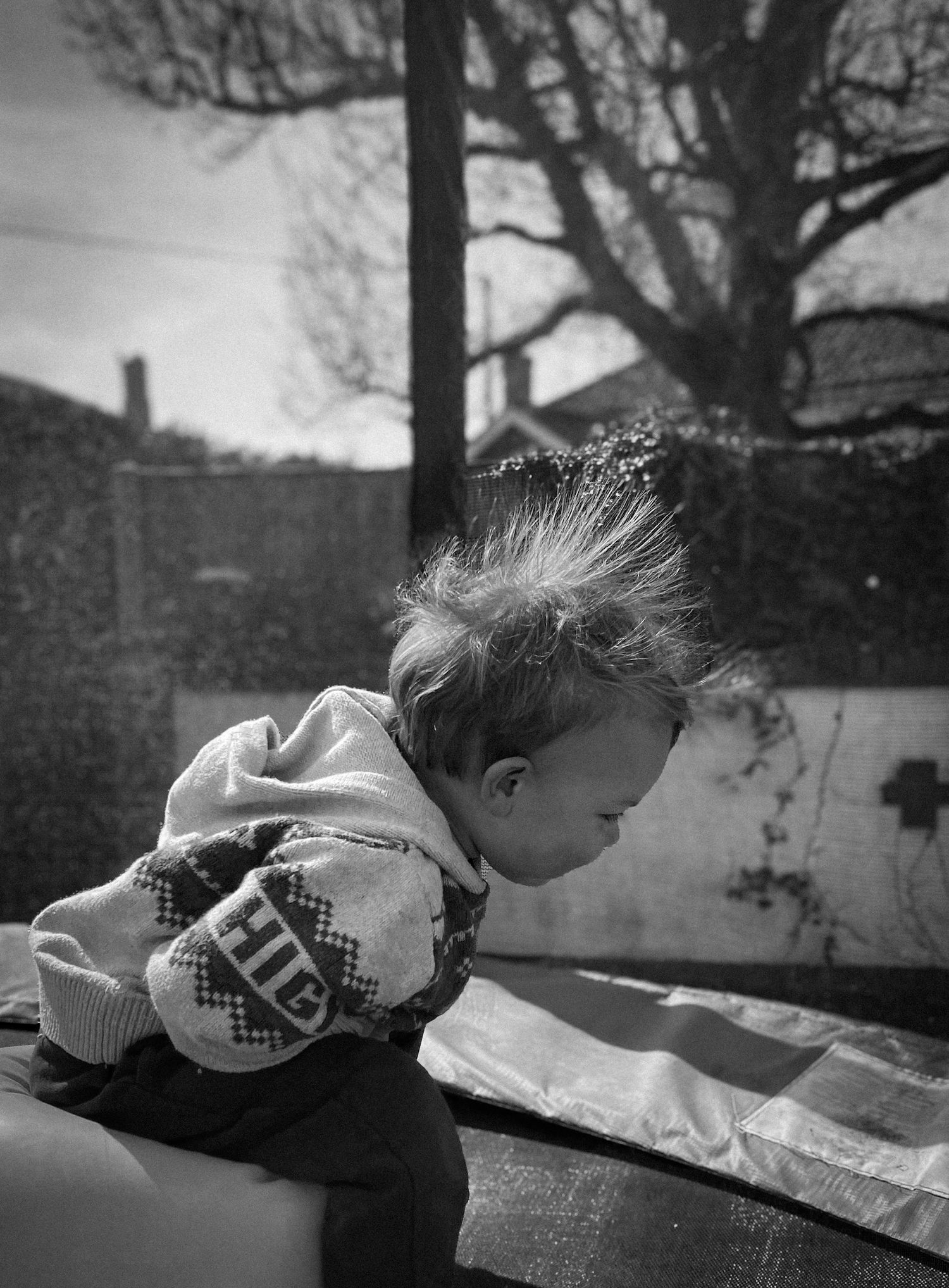 Young toddler in monochrome bending forward in outdoor setting.
