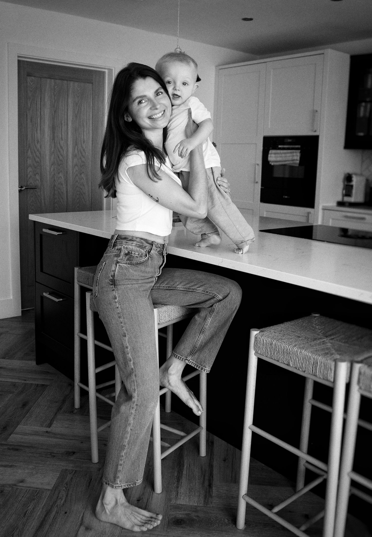 A black and white photo showing a casual moment in a modern kitchen with a baby and adult at a counter.
