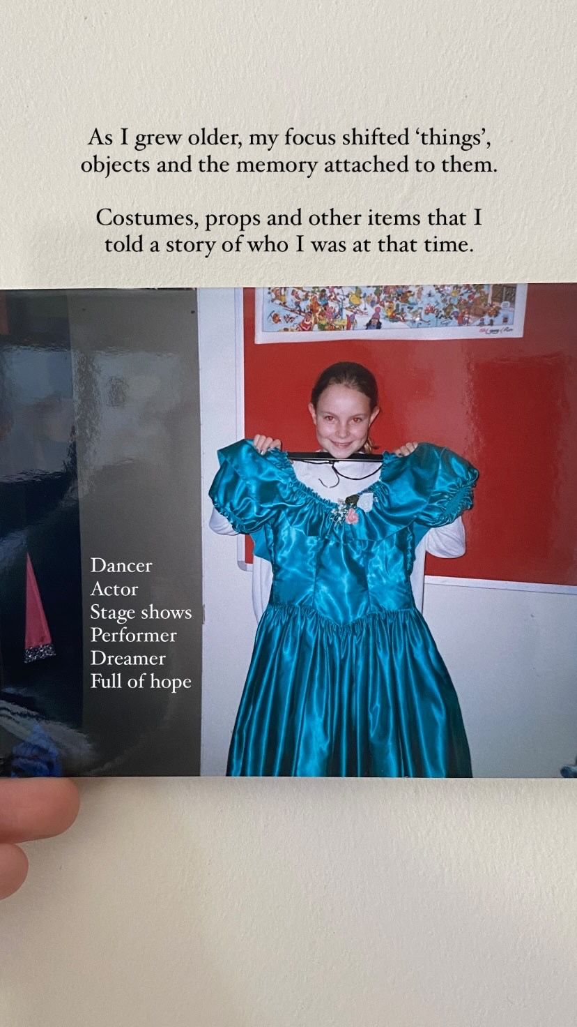 A person wearing a dramatic turquoise blue theatrical dress costume stands in front of a framed wall print.
