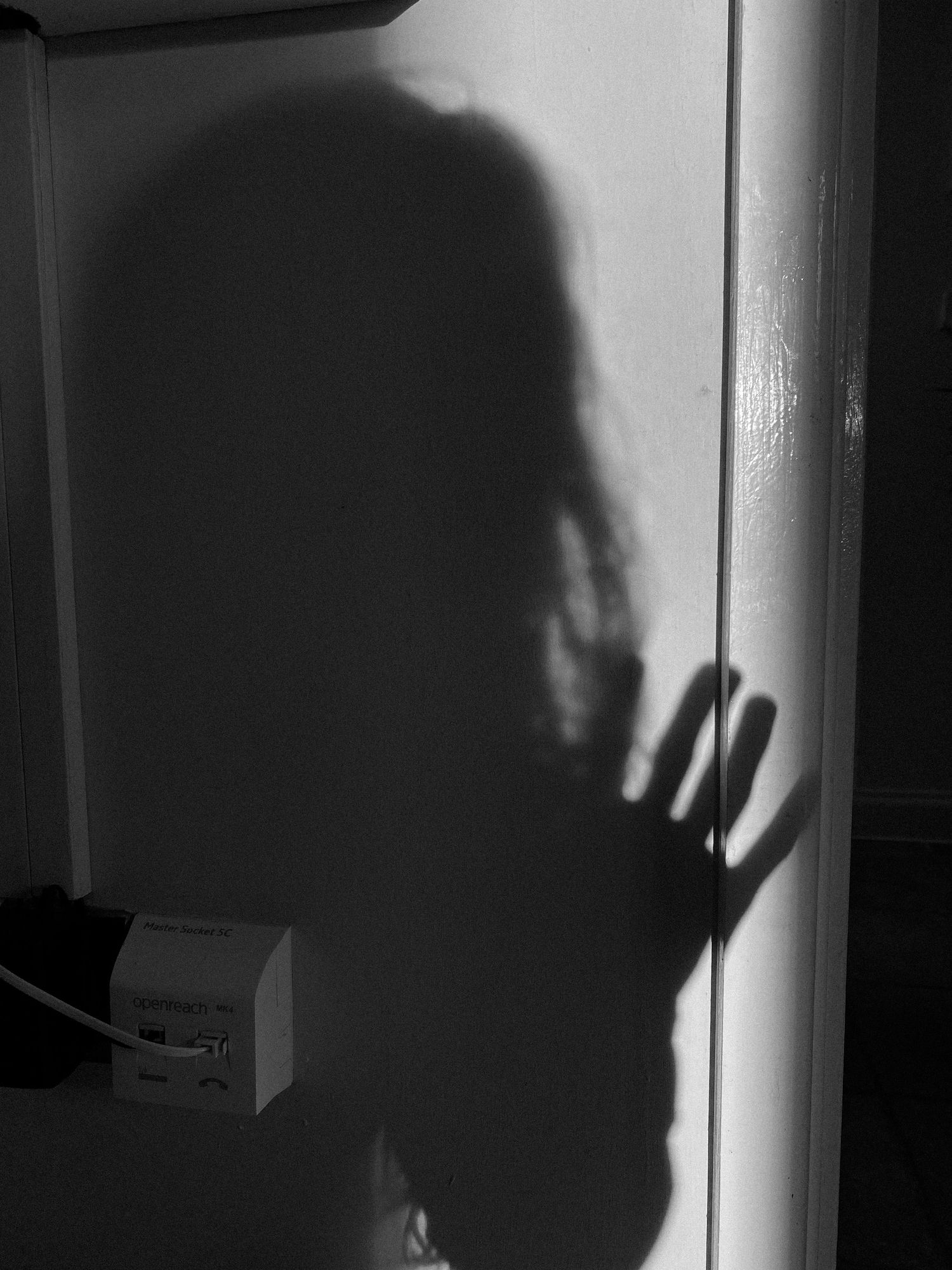 Dramatic black and white shadow of a hand against a white wall creating an eerie silhouette effect.
