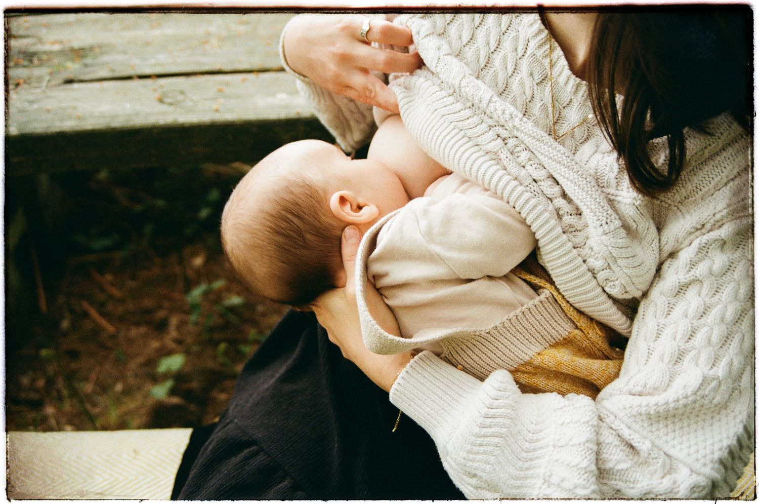 Small hands hold a tiny newborn baby wrapped in a cozy white knit blanket.