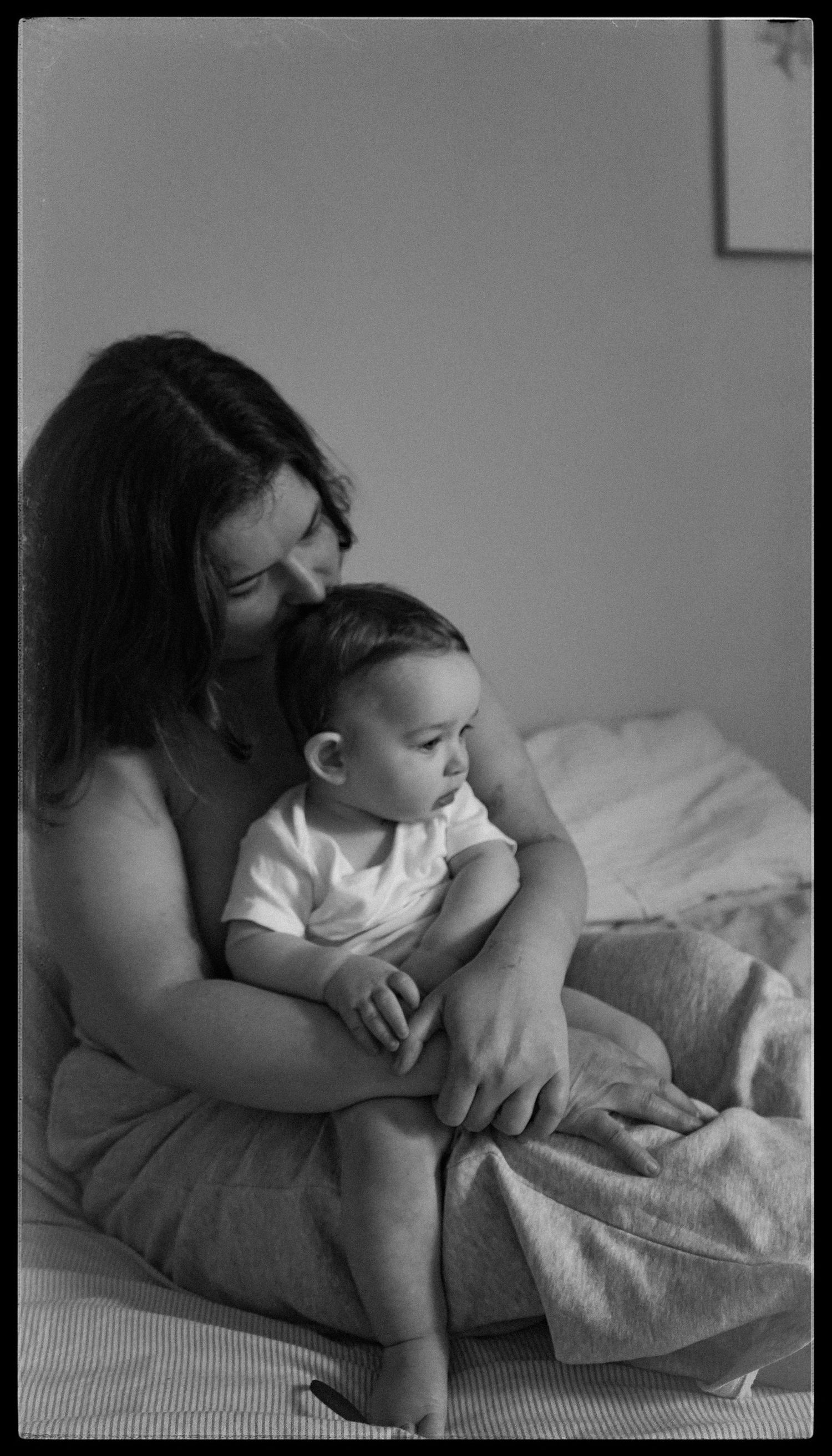 Intimate black and white portrait of parent holding infant on bed.