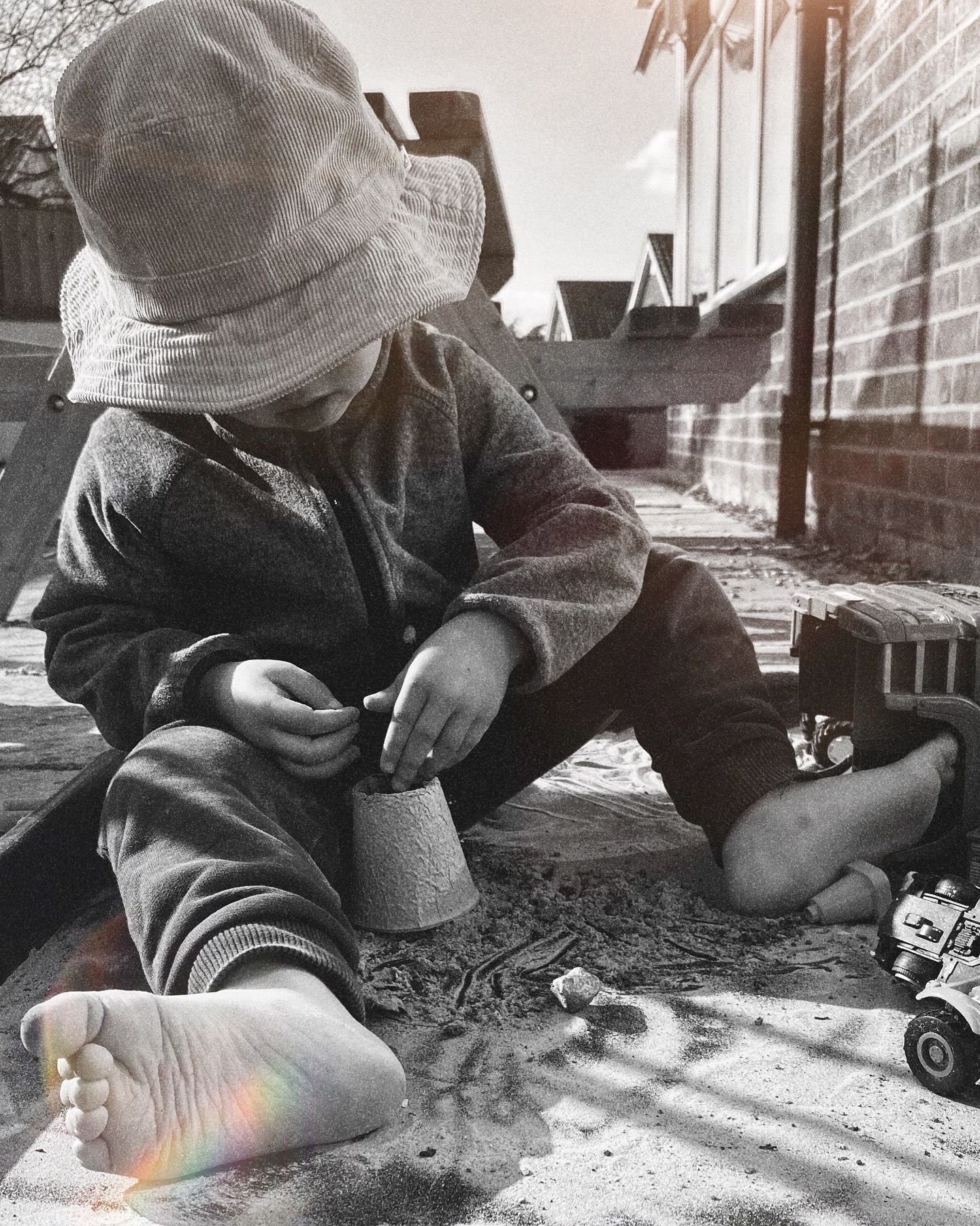 Child playing with toys on concrete in vintage-style black and white photography.