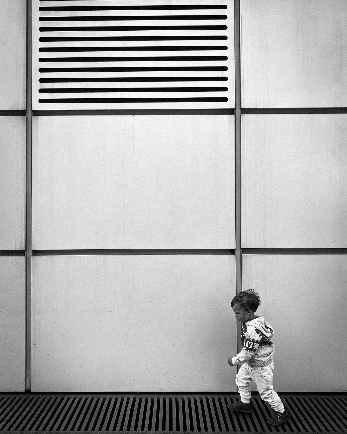 A small figure stands against a modern geometric wall with horizontal stripes.