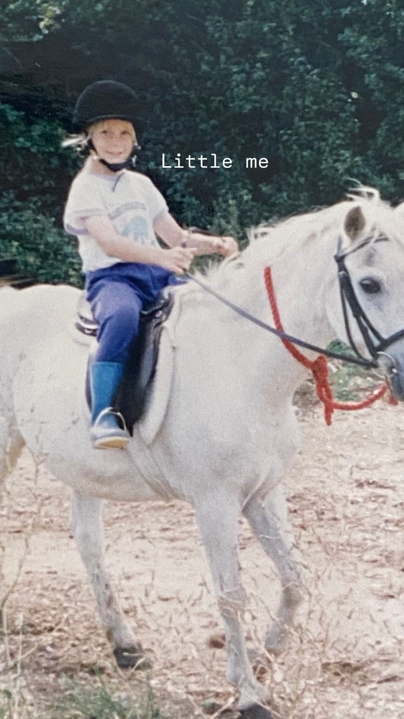 A rider sits atop a white horse during an outdoor riding lesson or trail ride.