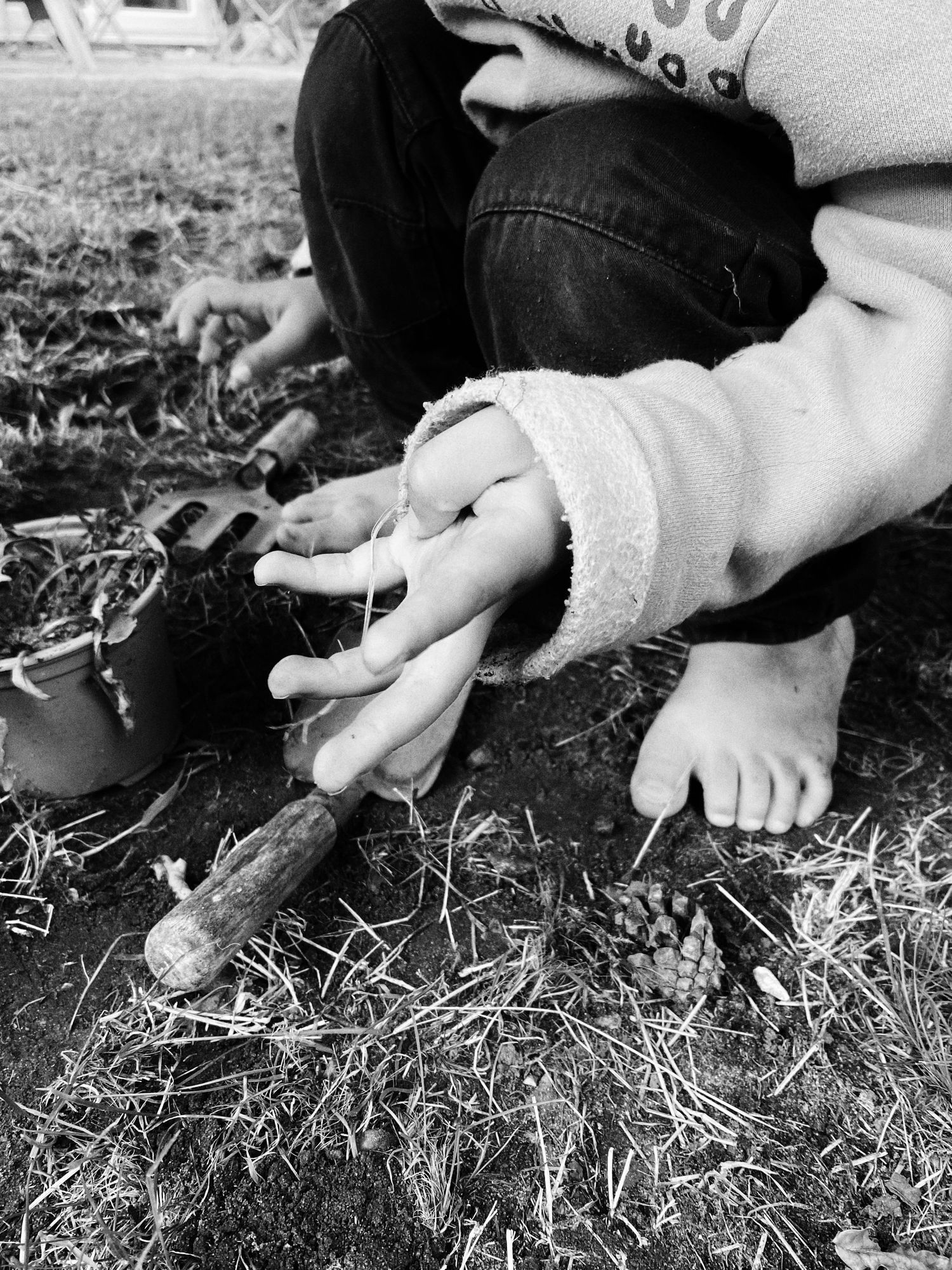 Child's hands and feet exploring grass and dried straw on the ground.