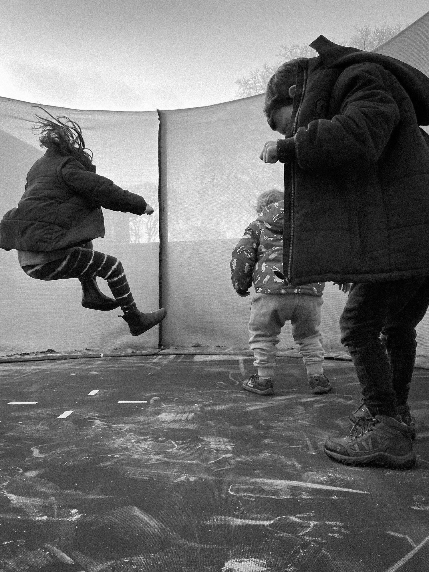Children playing and jumping on a snow-covered trampoline in winter.