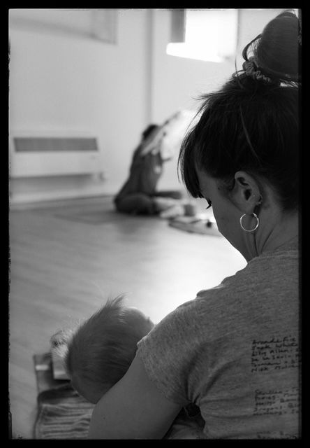 A black and white photograph of someone nursing a baby in a room with natural light from a window.