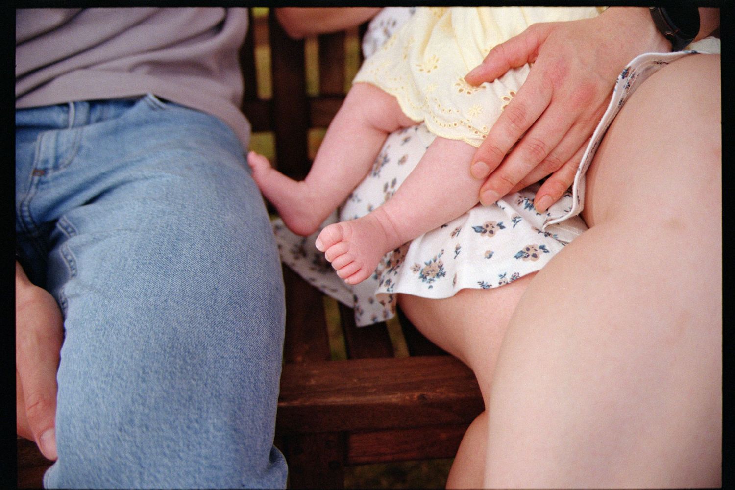 A person in blue denim holds a small baby wearing a white outfit.