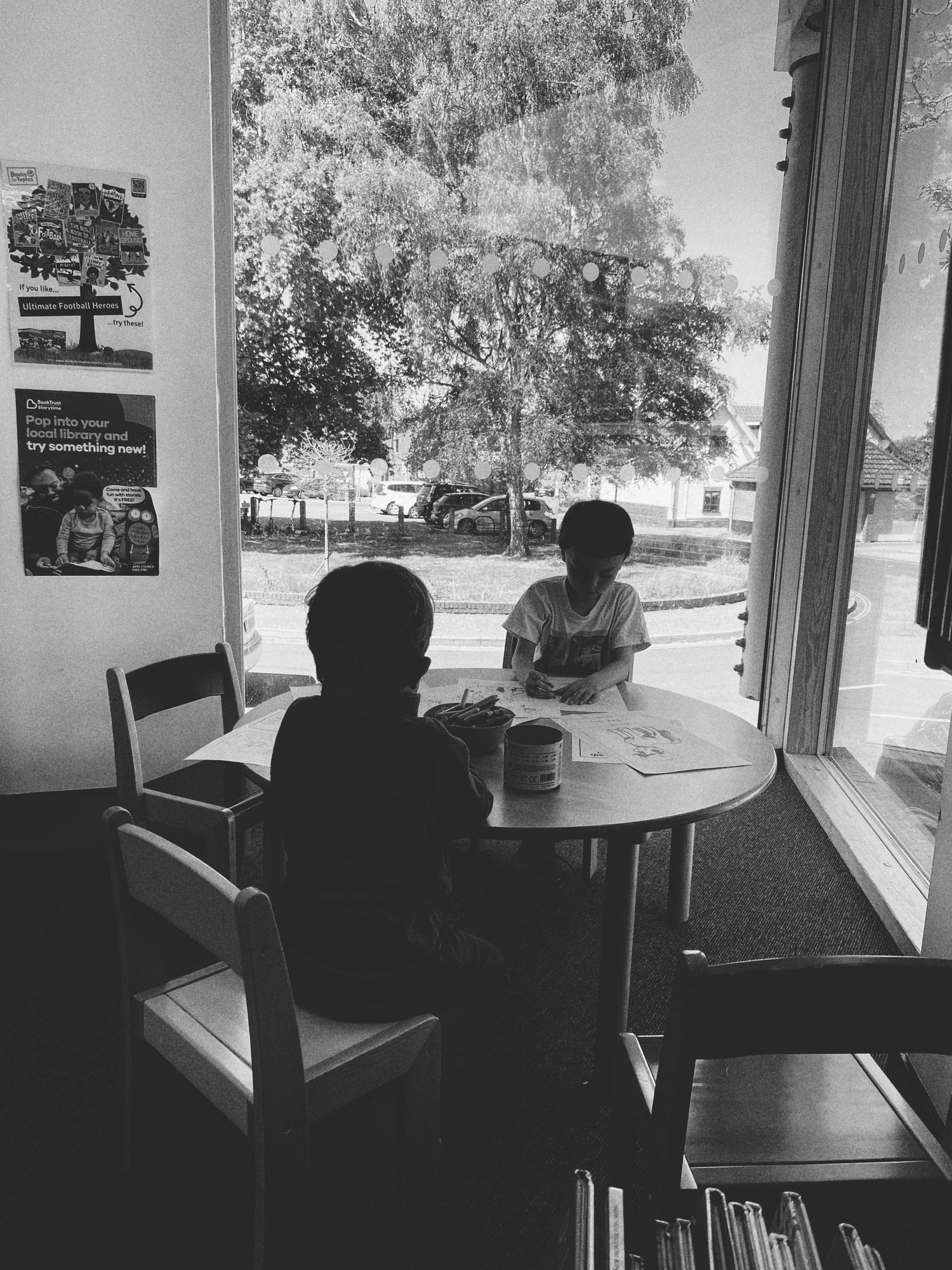 Two silhouettes sit at a round table near a window in a cafe setting.