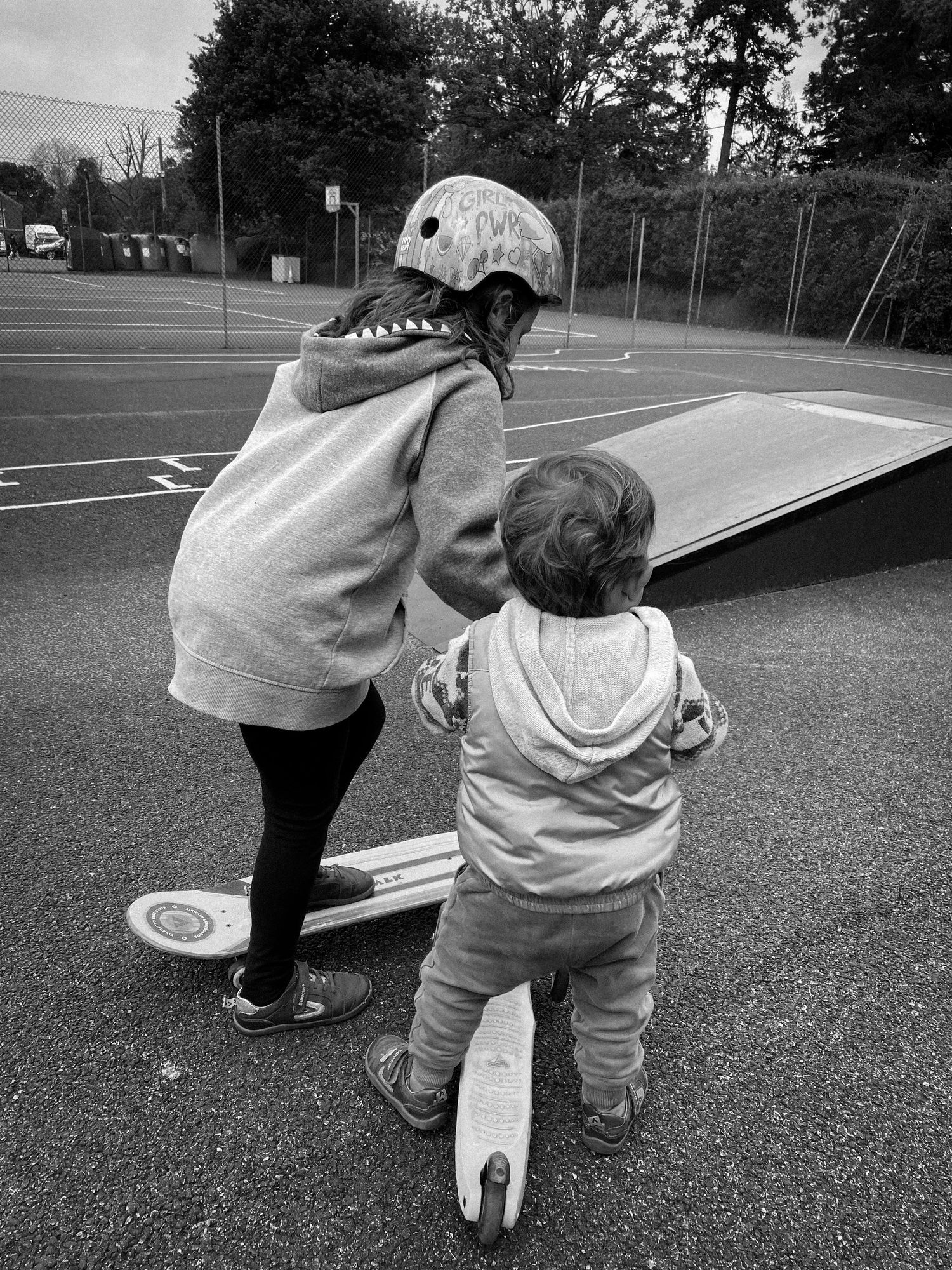 Two people practicing skateboarding on a ramp in an empty parking lot.