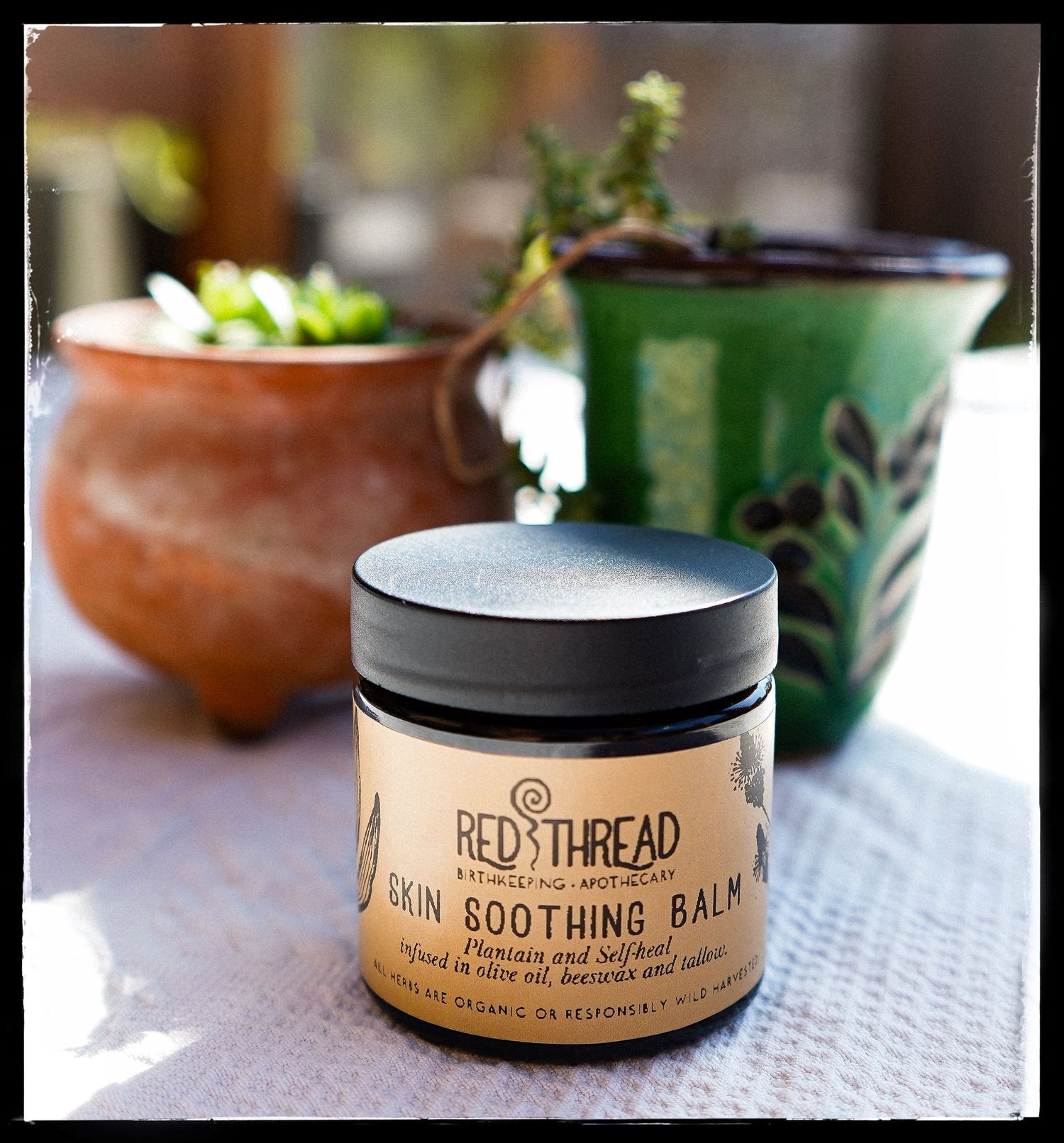 Close up product photography of Red Thread and Soothing Balm skin care containers arranged on a white surface.