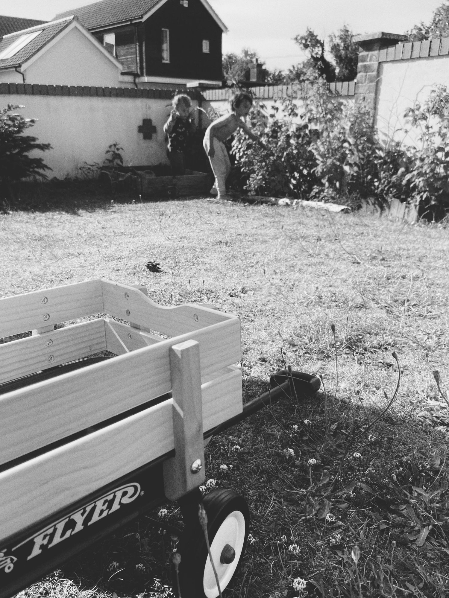 A Radio Flyer wagon sits in a backyard garden with people gardening in the background.