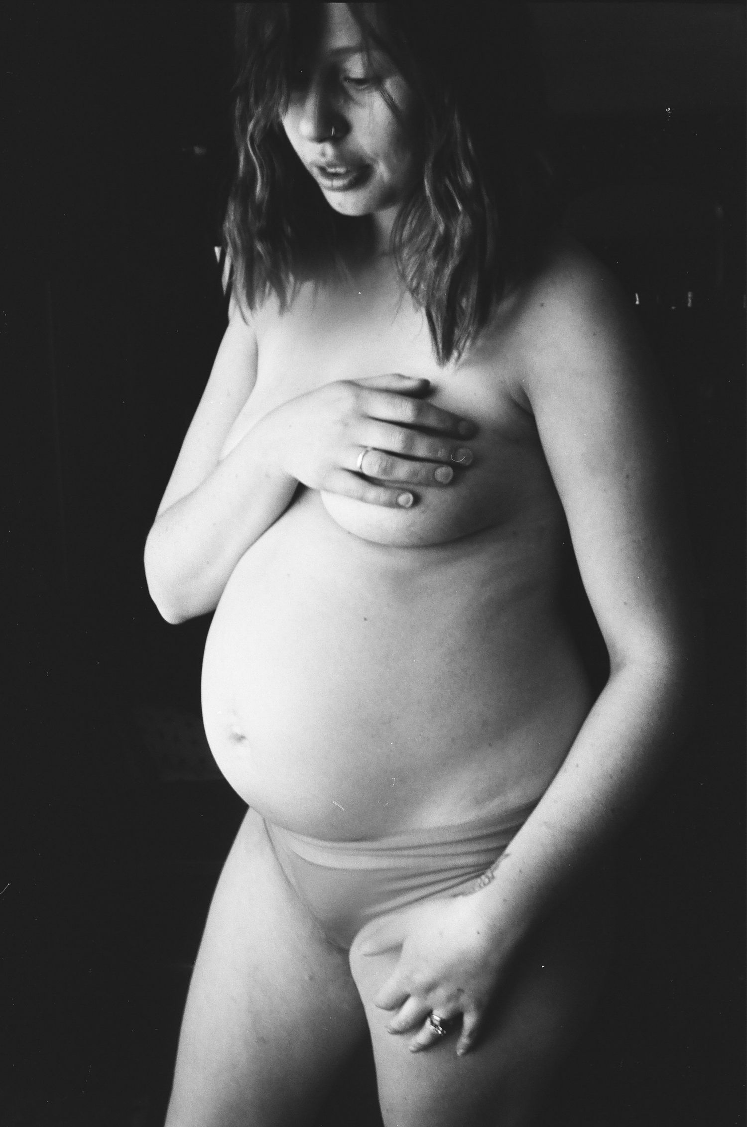 Artistic black and white portrait of an expectant figure in intimate lighting.