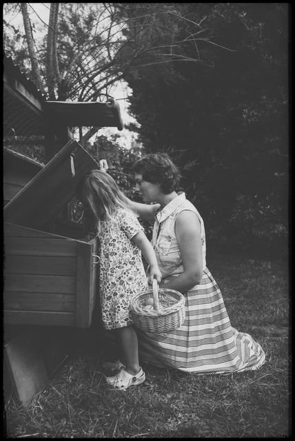 Vintage black and white photo of two people in a backyard with a basket near a garden shed.