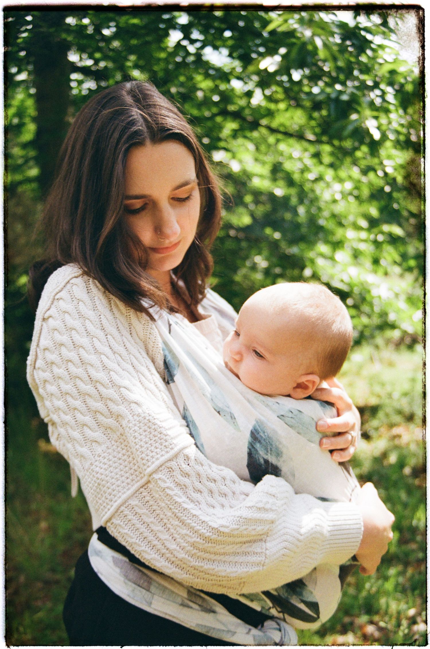 Parent and baby sharing a sweet moment outdoors in white knit sweater against green background.