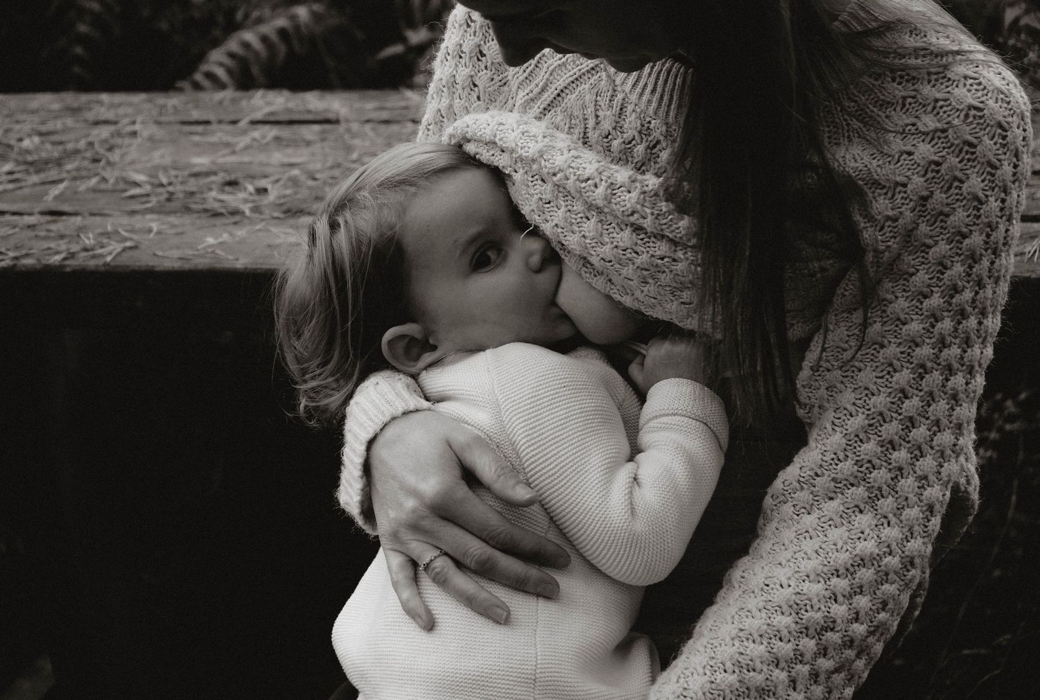 Intimate black and white photograph capturing nurturing moment between parent and child outdoors.
