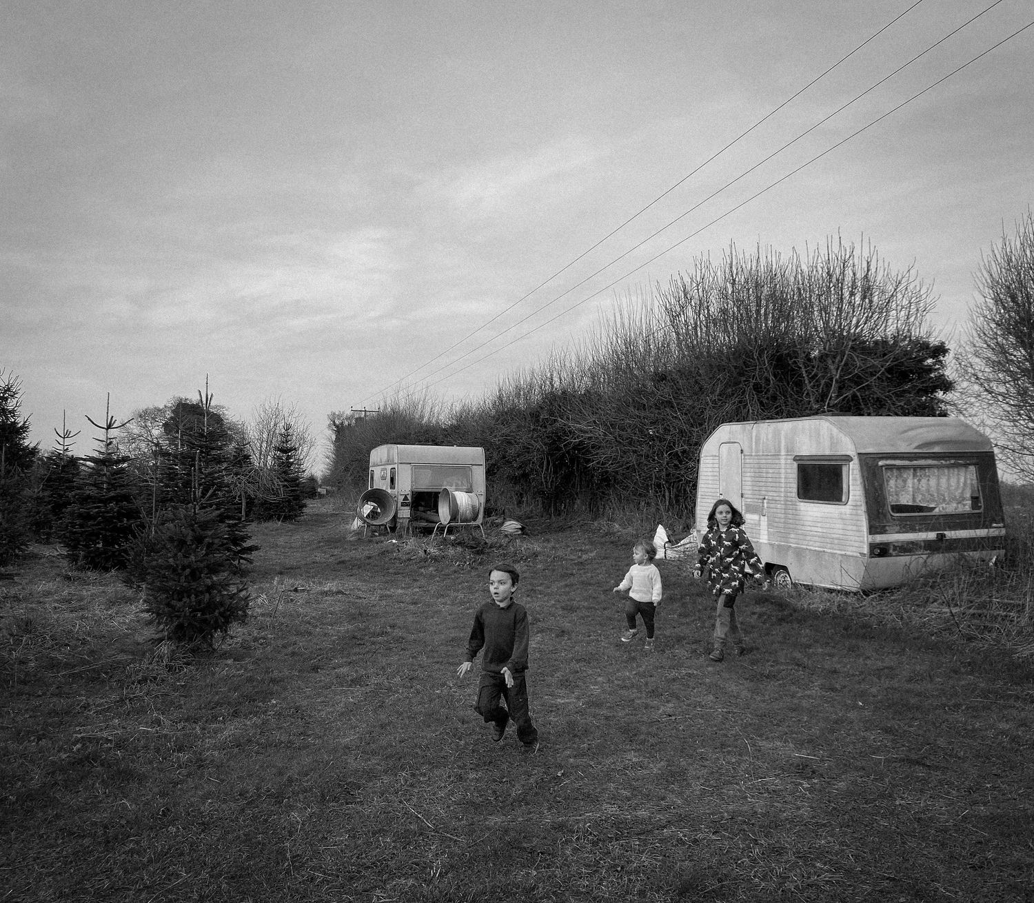 Children playing near vintage caravans in a field with bare trees in the background.