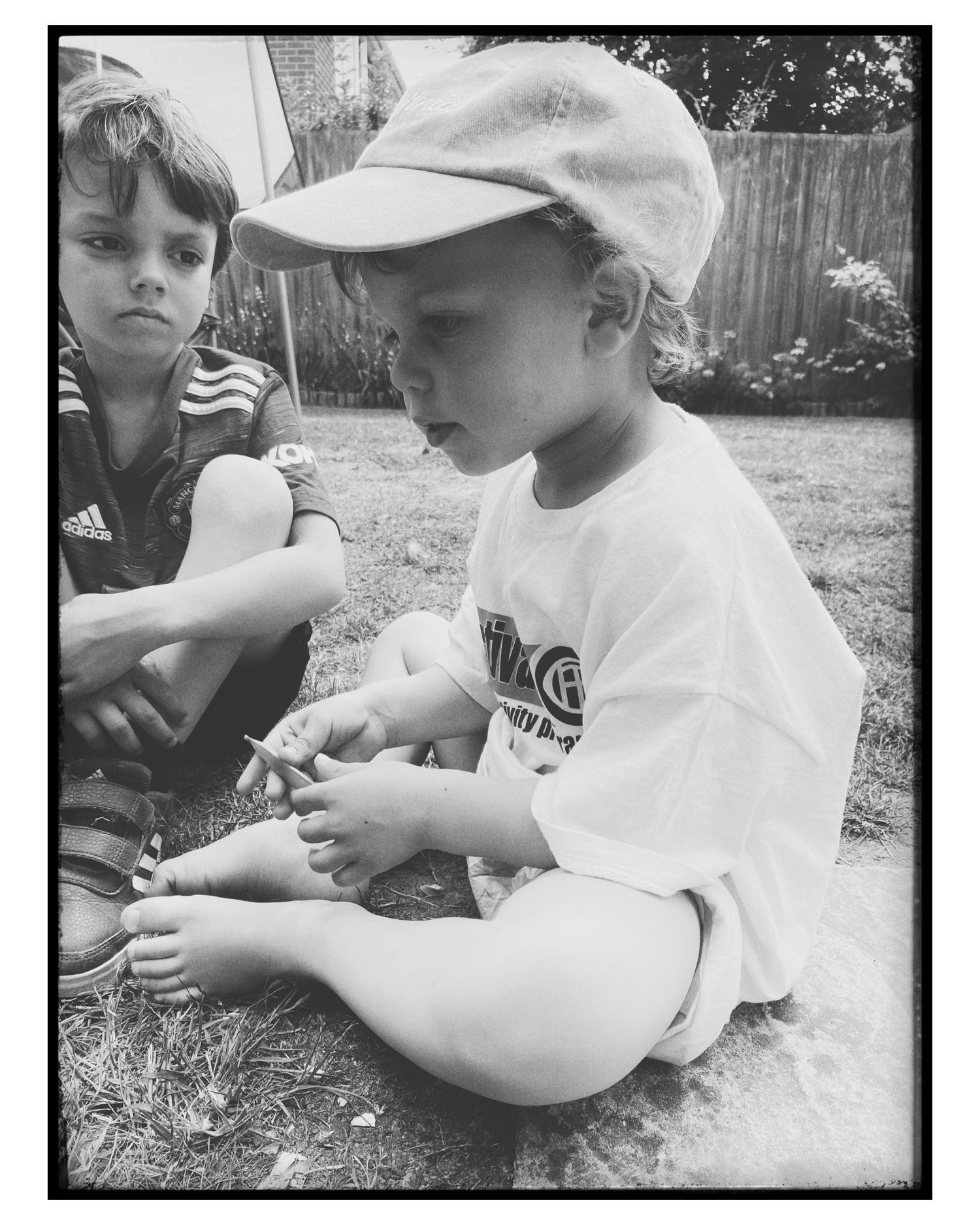 Children sitting in grass examining something in their hands during summer.