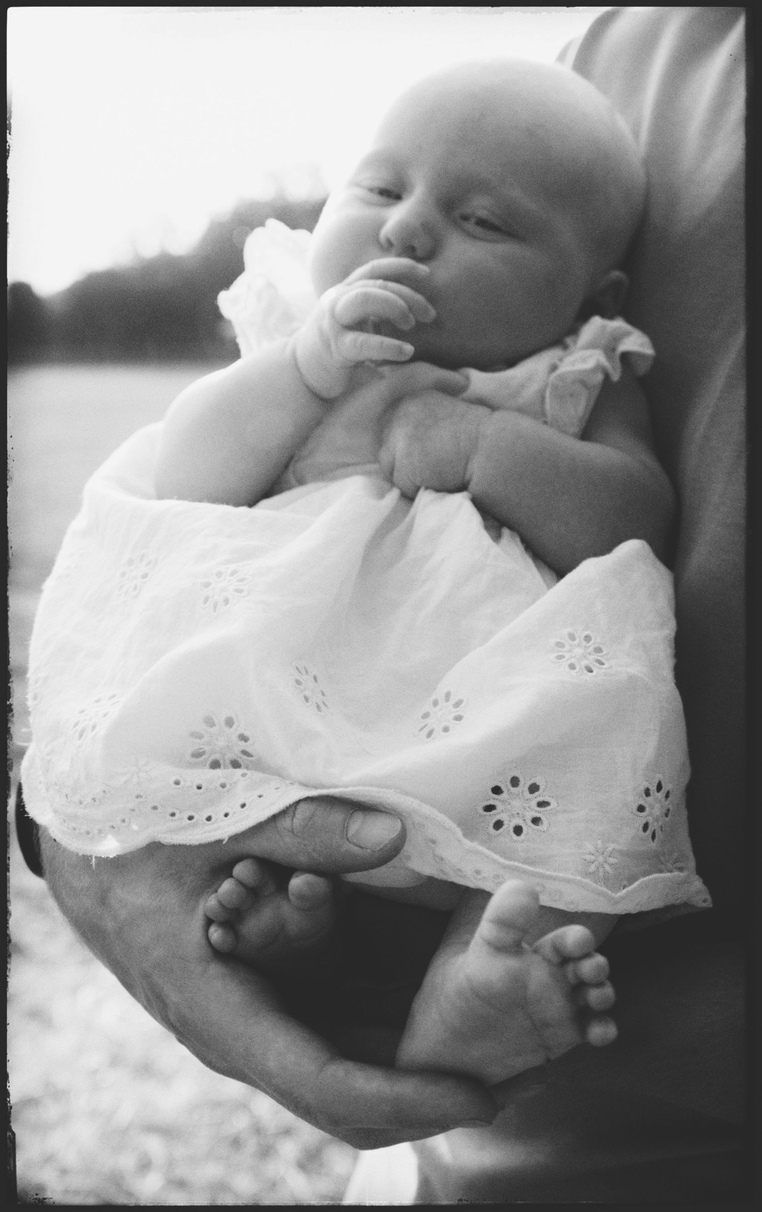 Black and white series of photos showing a baby wearing a white eyelet dress being gently cradled.