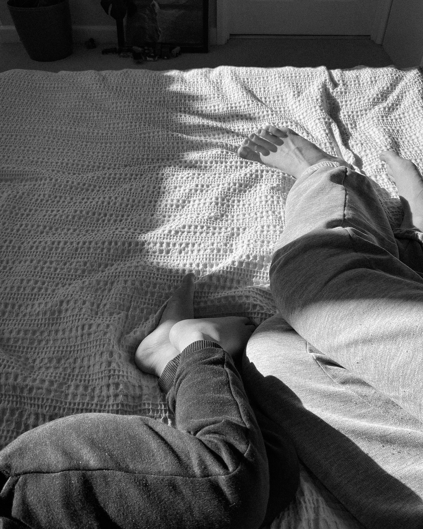 Person lying down on a white textured bedspread in black and white photography.