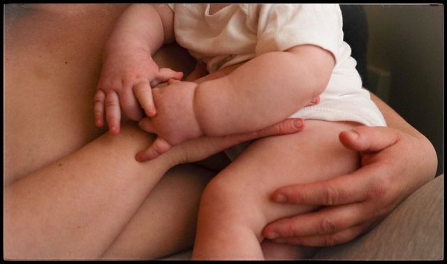Adult hands gently hold tiny baby feet and toes in a tender close-up photograph.