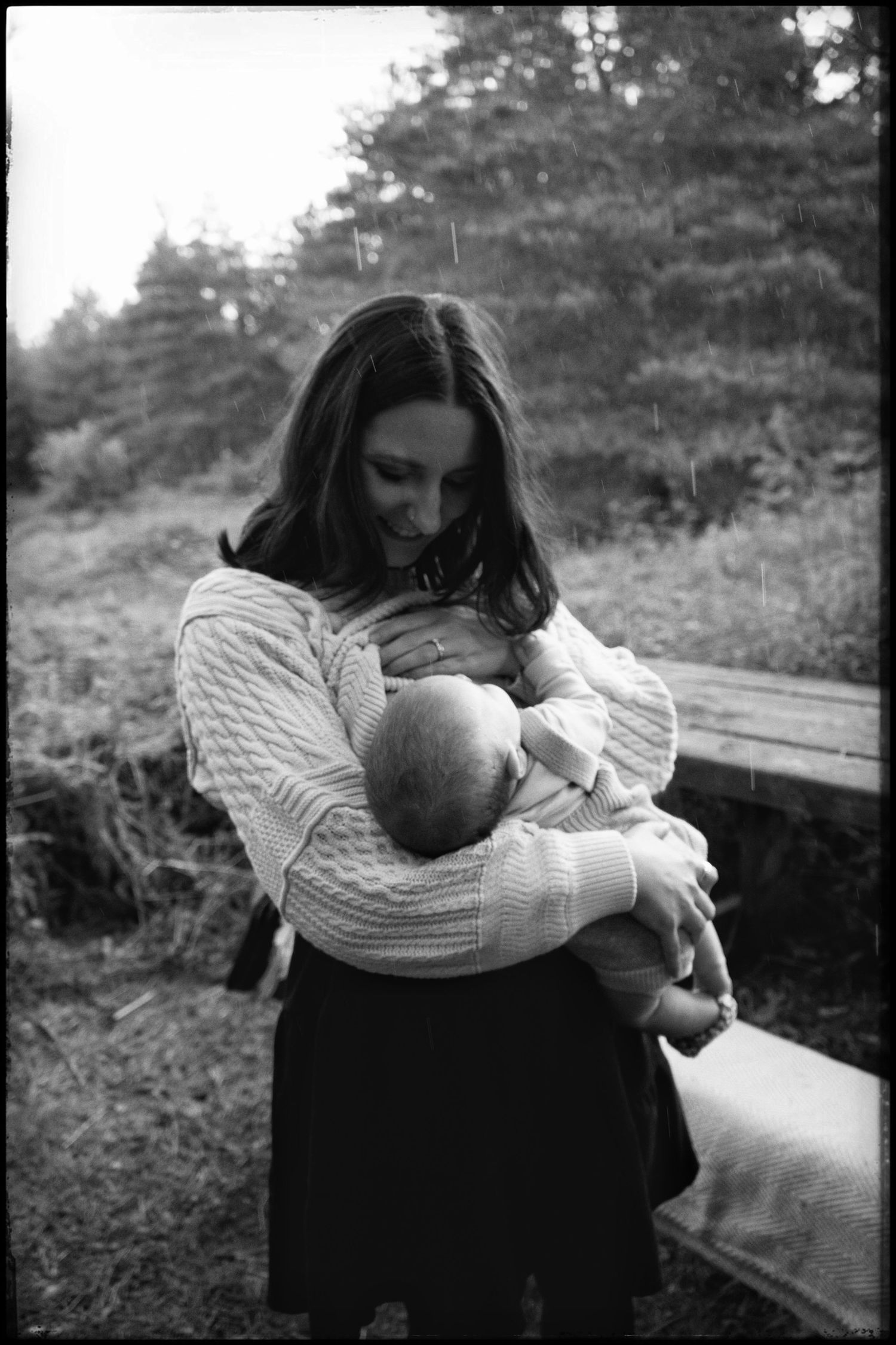 A tender black and white photograph of breastfeeding in a peaceful outdoor setting among trees.
