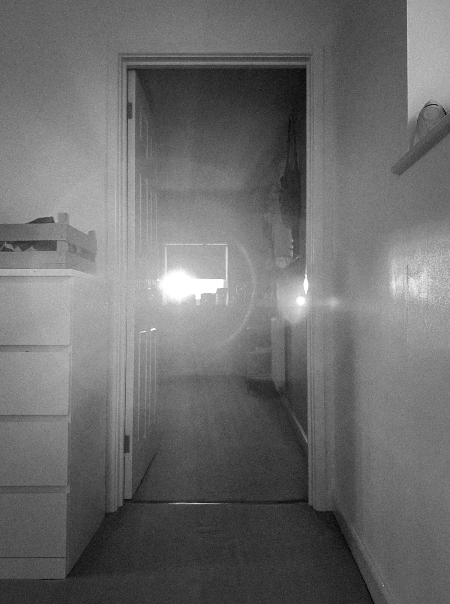 Bright light illuminates a doorway at the end of a stark hallway.