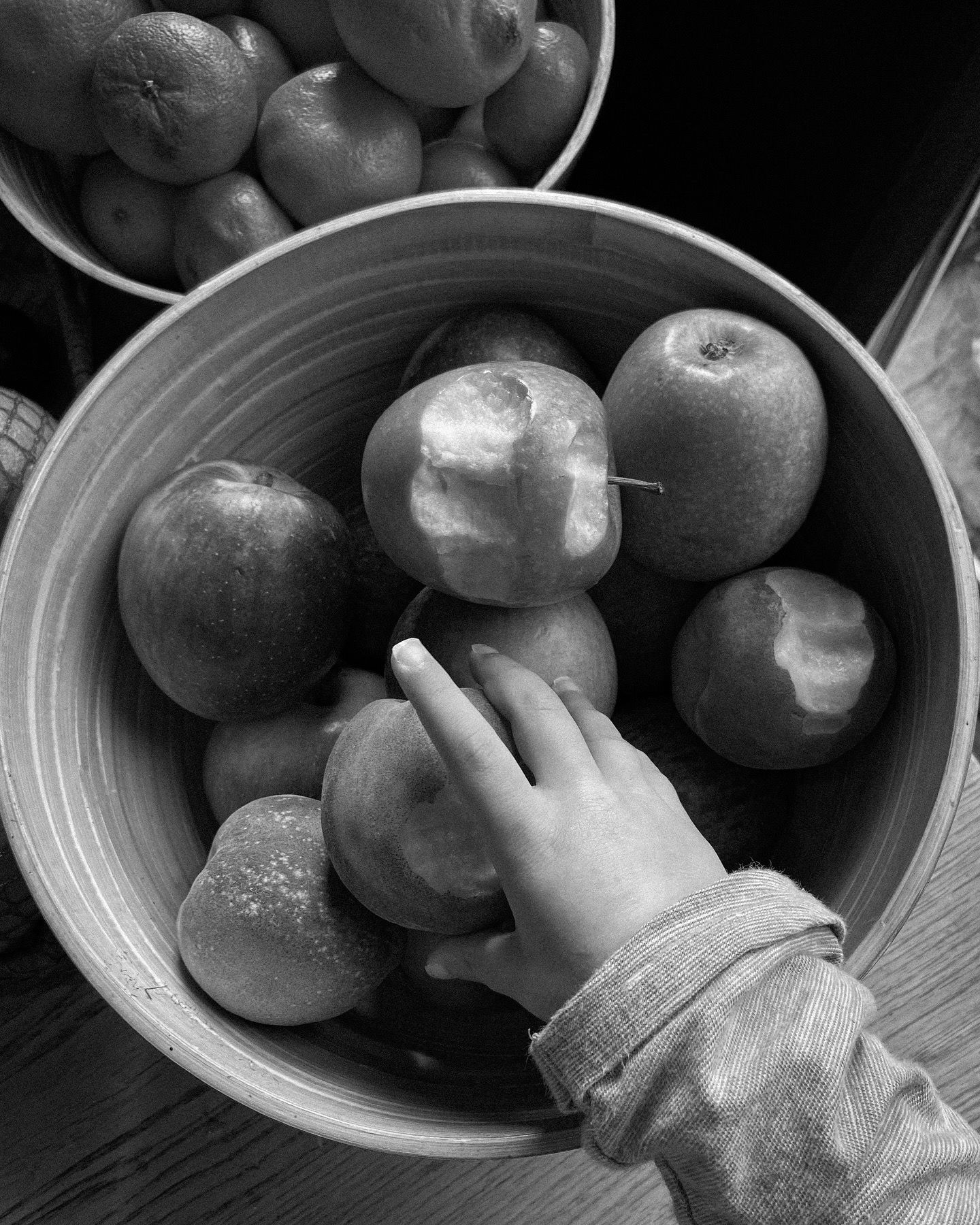 Small hand reaching for fresh apples in a ceramic bowl shot in black and white.