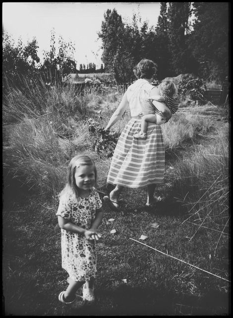 Vintage black and white photograph showing people outdoors in tall grass and trees during summer.