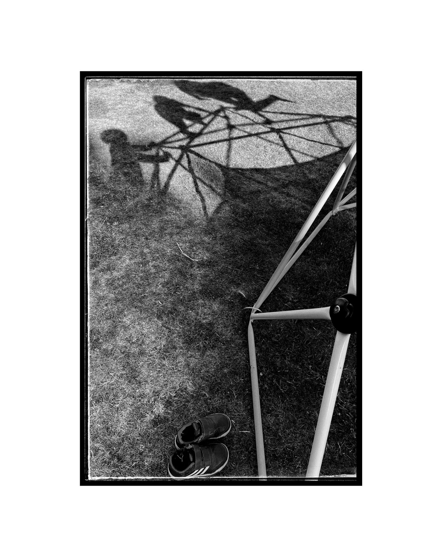 Shadow cast on concrete with bicycle frame and shoes visible in stark monochrome composition.