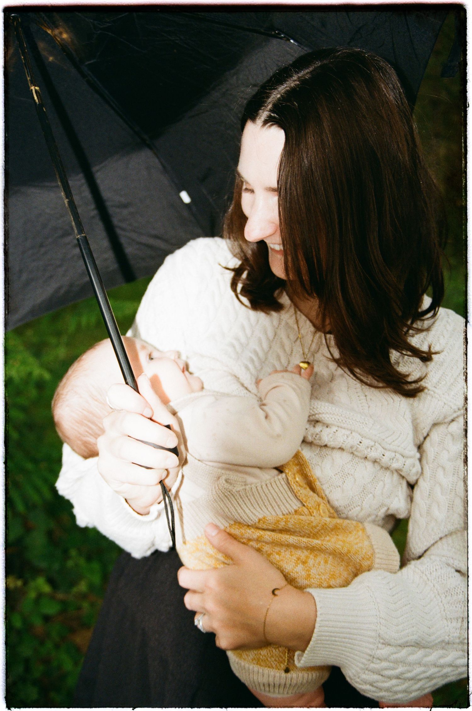 A person in a cream cable knit sweater holds a black umbrella while standing outdoors on a rainy day.