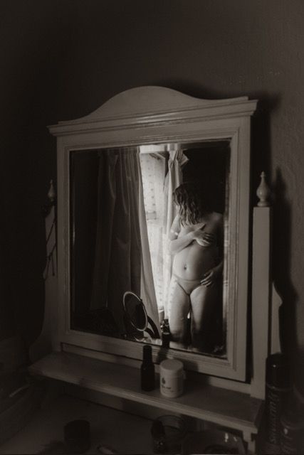 Artistic black and white photo reflection in vintage vanity mirror with moody lighting.