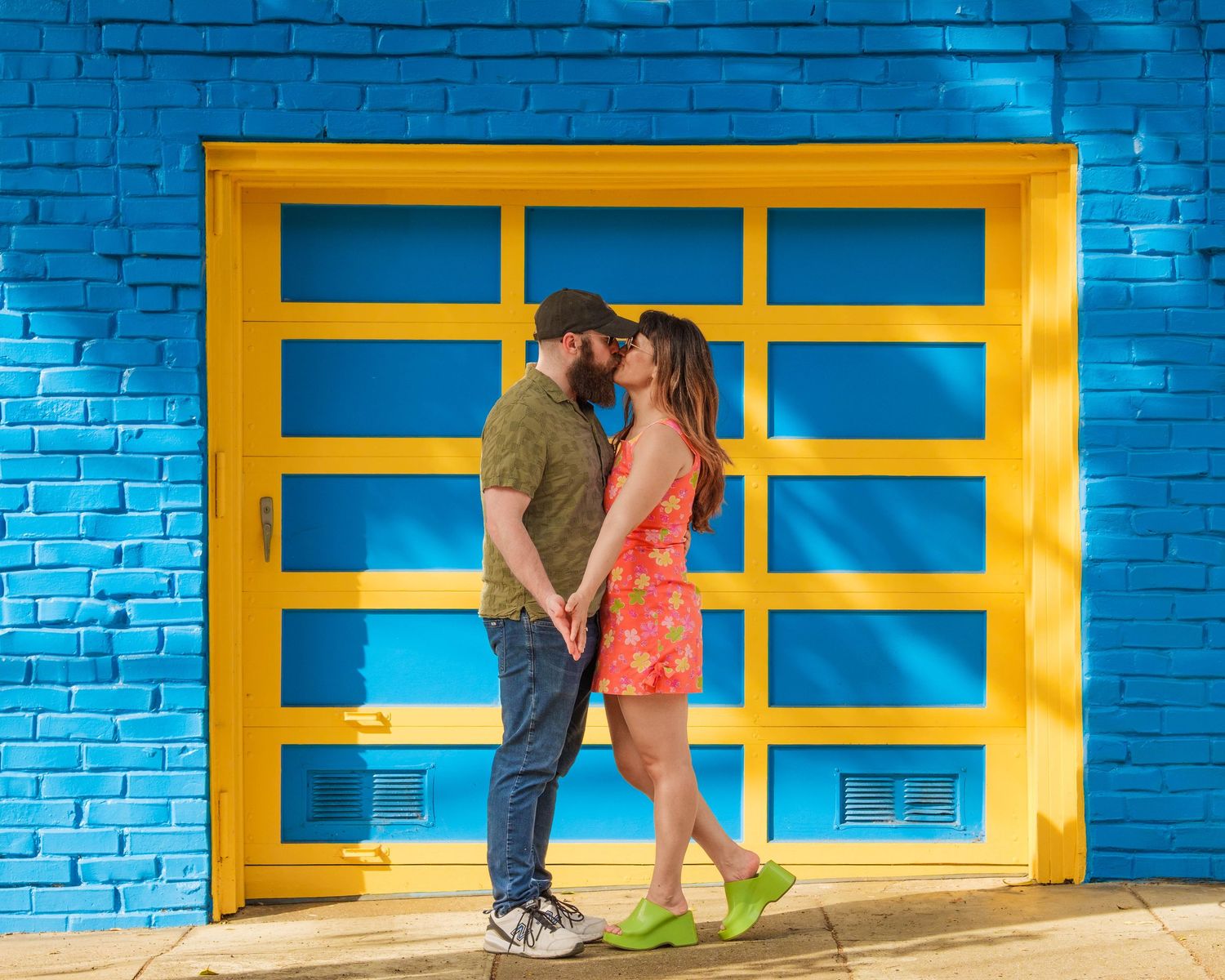 a happy couple recently engaged in san francisco. they are kissing in front of a vibrant blue and yellow garage door