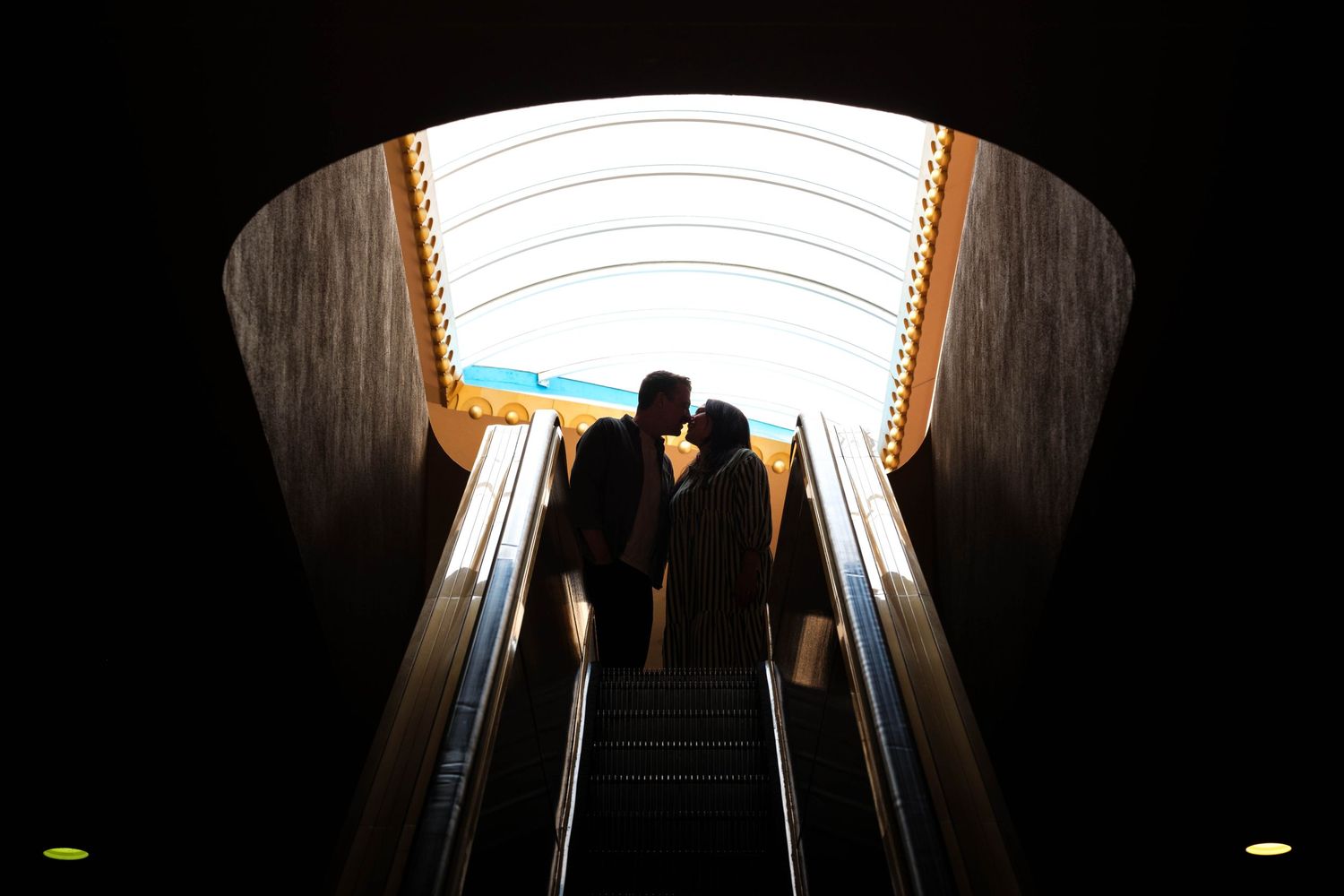 a photo of a happy couple recently engaged, kissing at the escalator of the marin county civic center