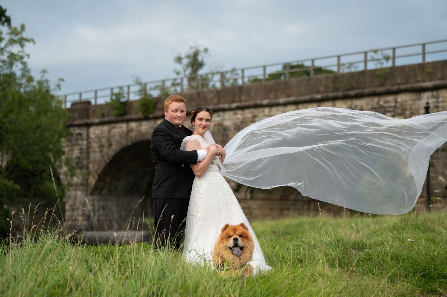 Bride’s veil caught in the wind as the couple pose near a viaduct