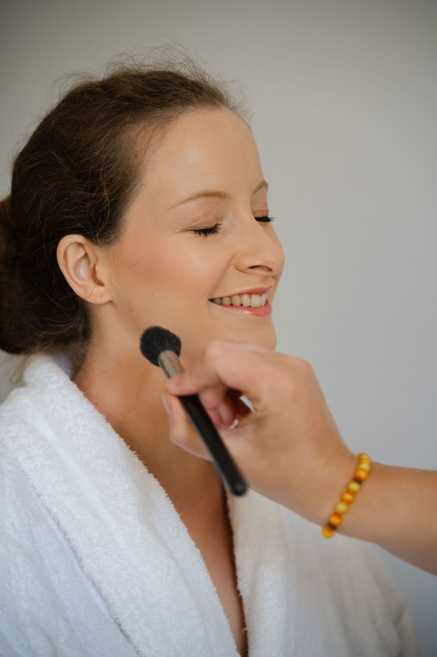 Bride getting her makeup done, smiling while a brush is applied to her cheek