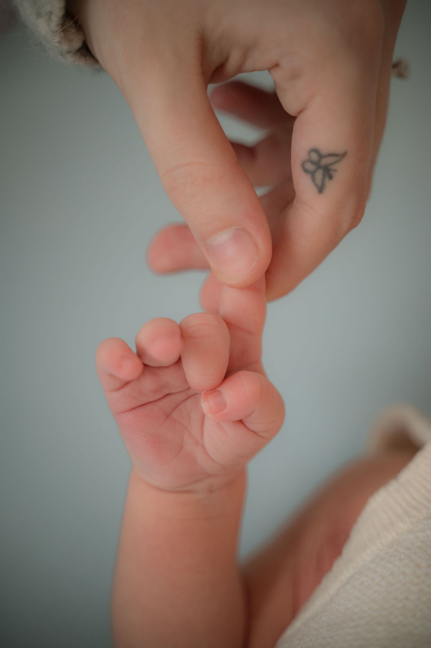 Close-up of a newborn’s hand tightly grasping an adult’s tattooed finger, symbolizing connection and care.