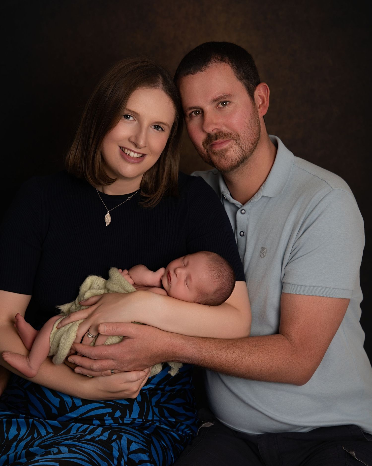 New parents holding their newborn baby close during an in-home family photography session, capturing early bonding and connection.