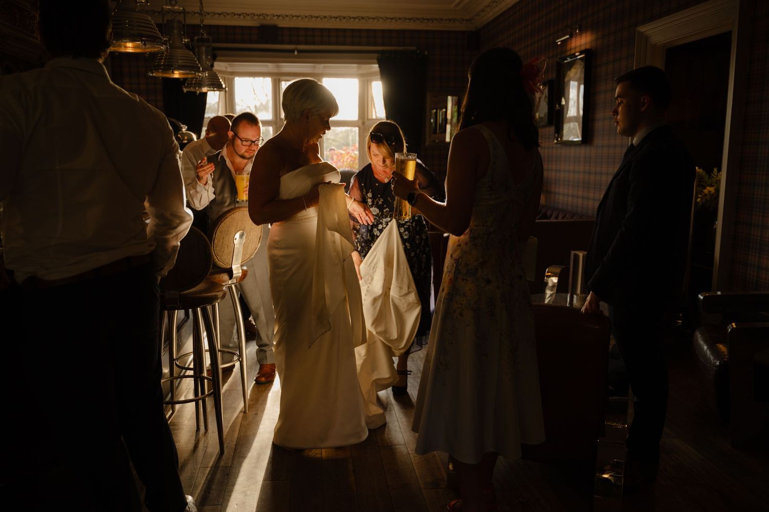 Bride entering the wedding reception room to a warm welcome from guests, walking in with excitement under moody golden lighting.