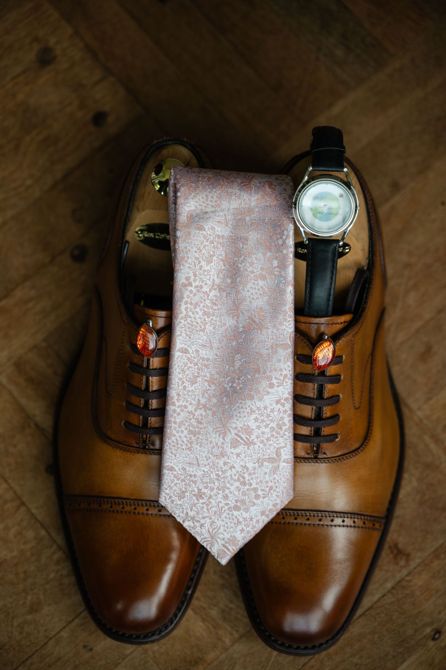 Flat lay of brown leather wedding shoes with floral tie placed neatly in between