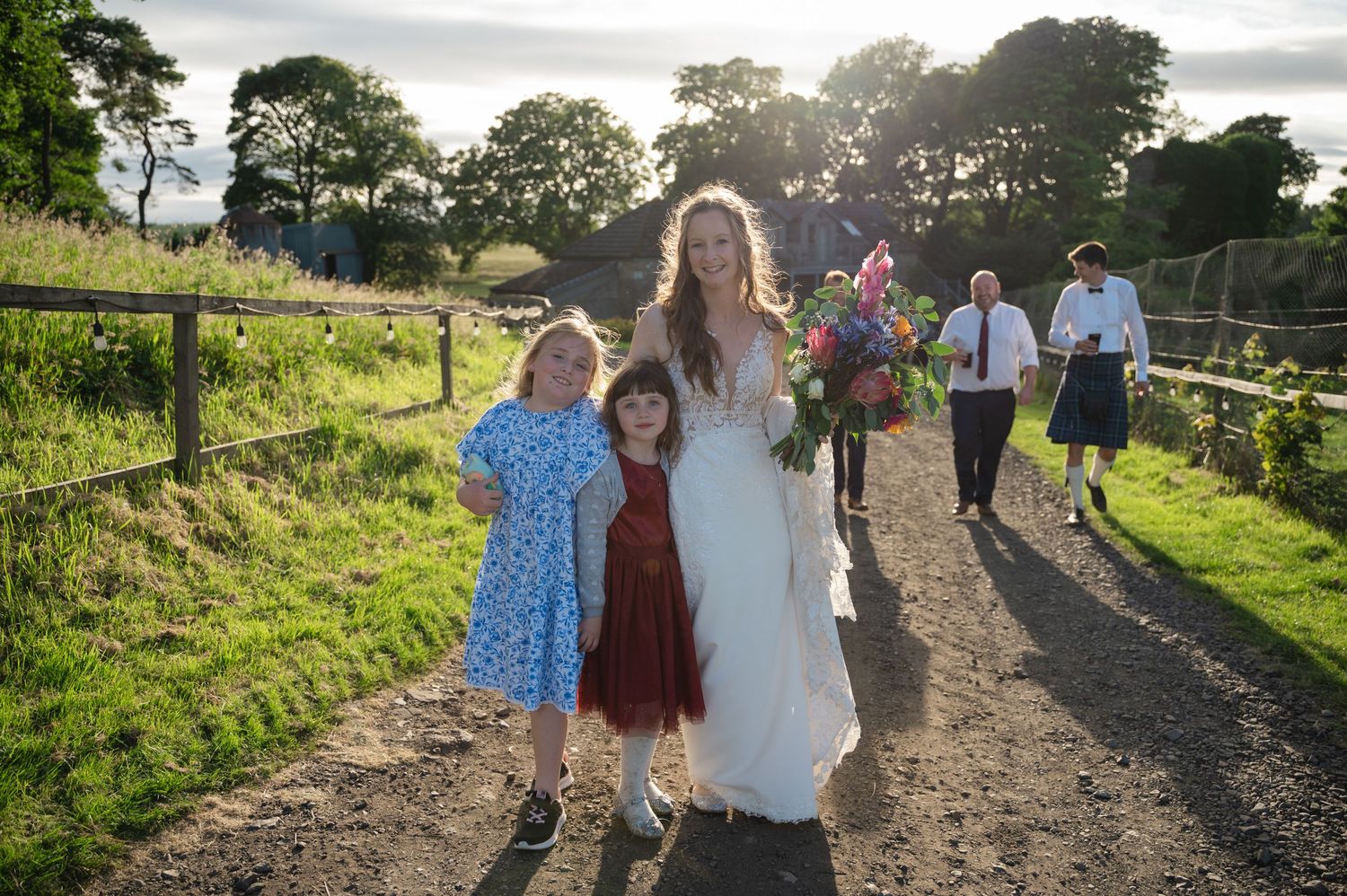 Bride walking with children and guests along rural path during relaxed wedding