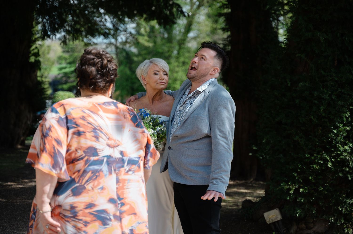 Bride and groom chatting outdoors with a casually dressed guest.