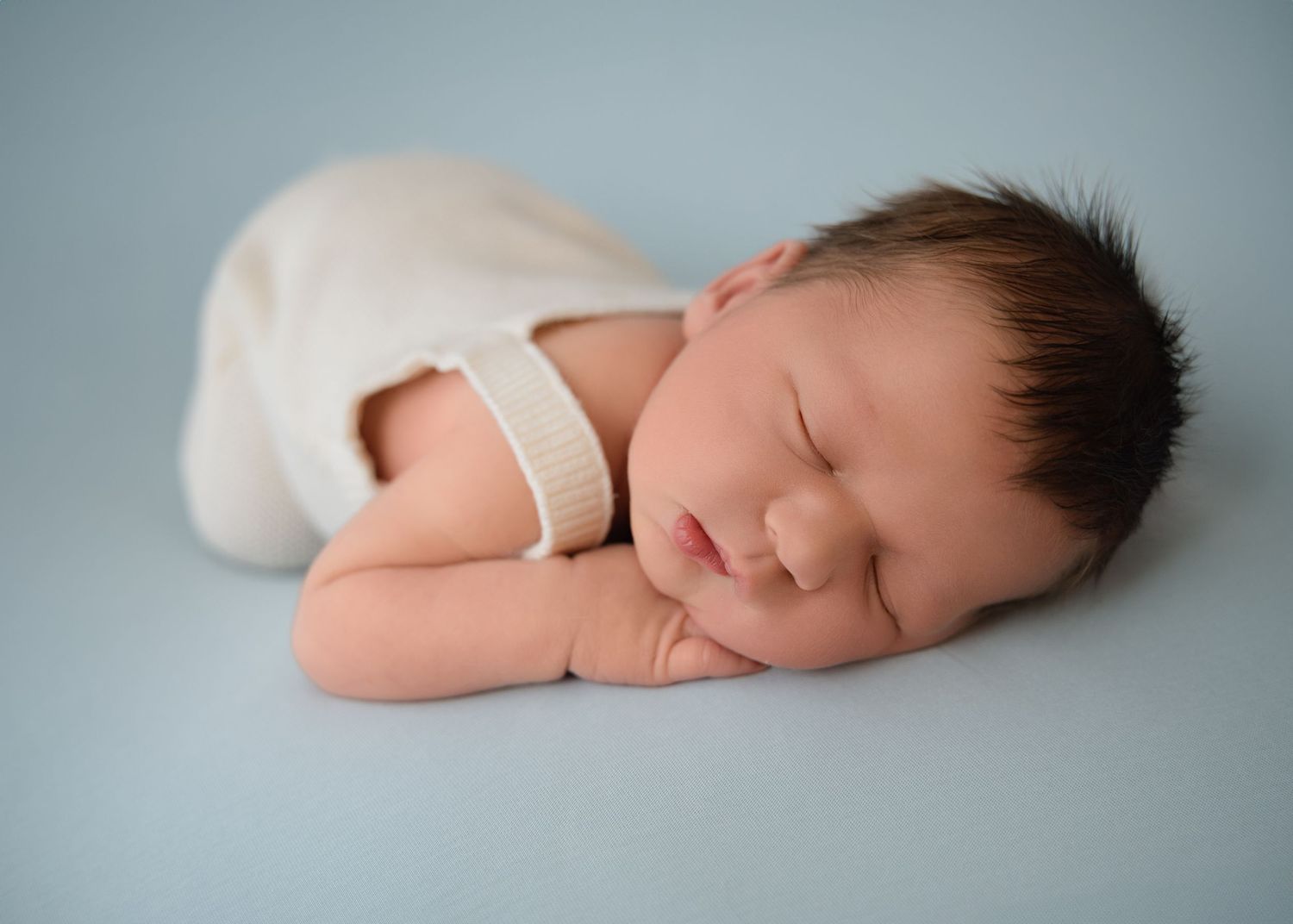 Sleeping newborn wrapped in soft white blanket on light blue background – simple, classic newborn portrait