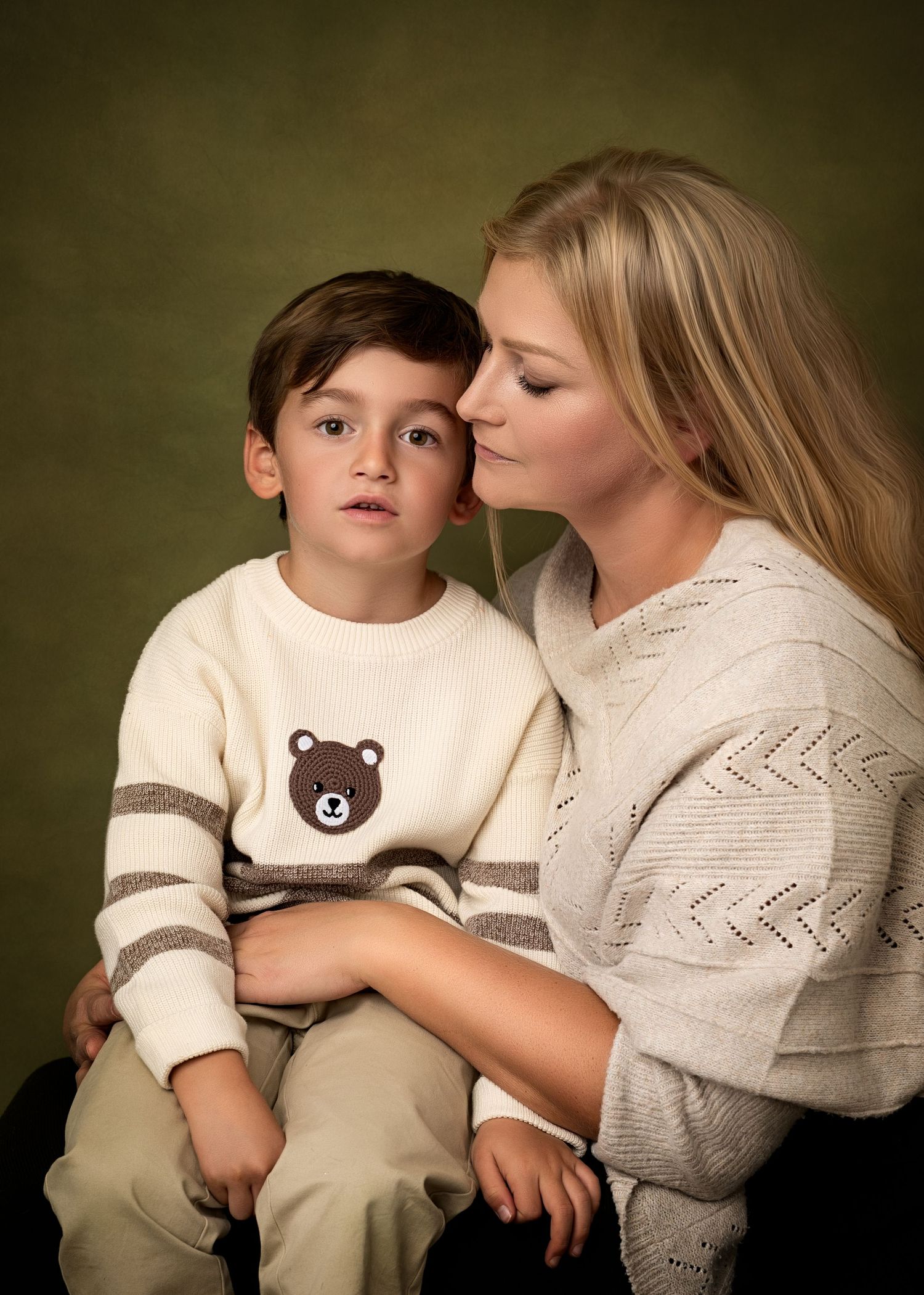 Fine art mother and son portrait with a dark green backdrop, the mother lovingly looking at her son
