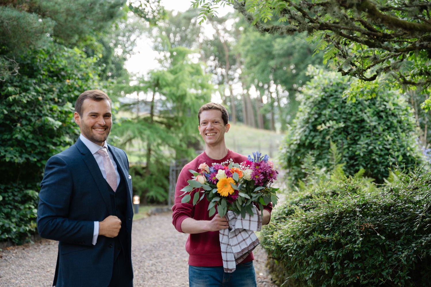 Groom smiling with a guest holding the wedding bouquet in a garden setting