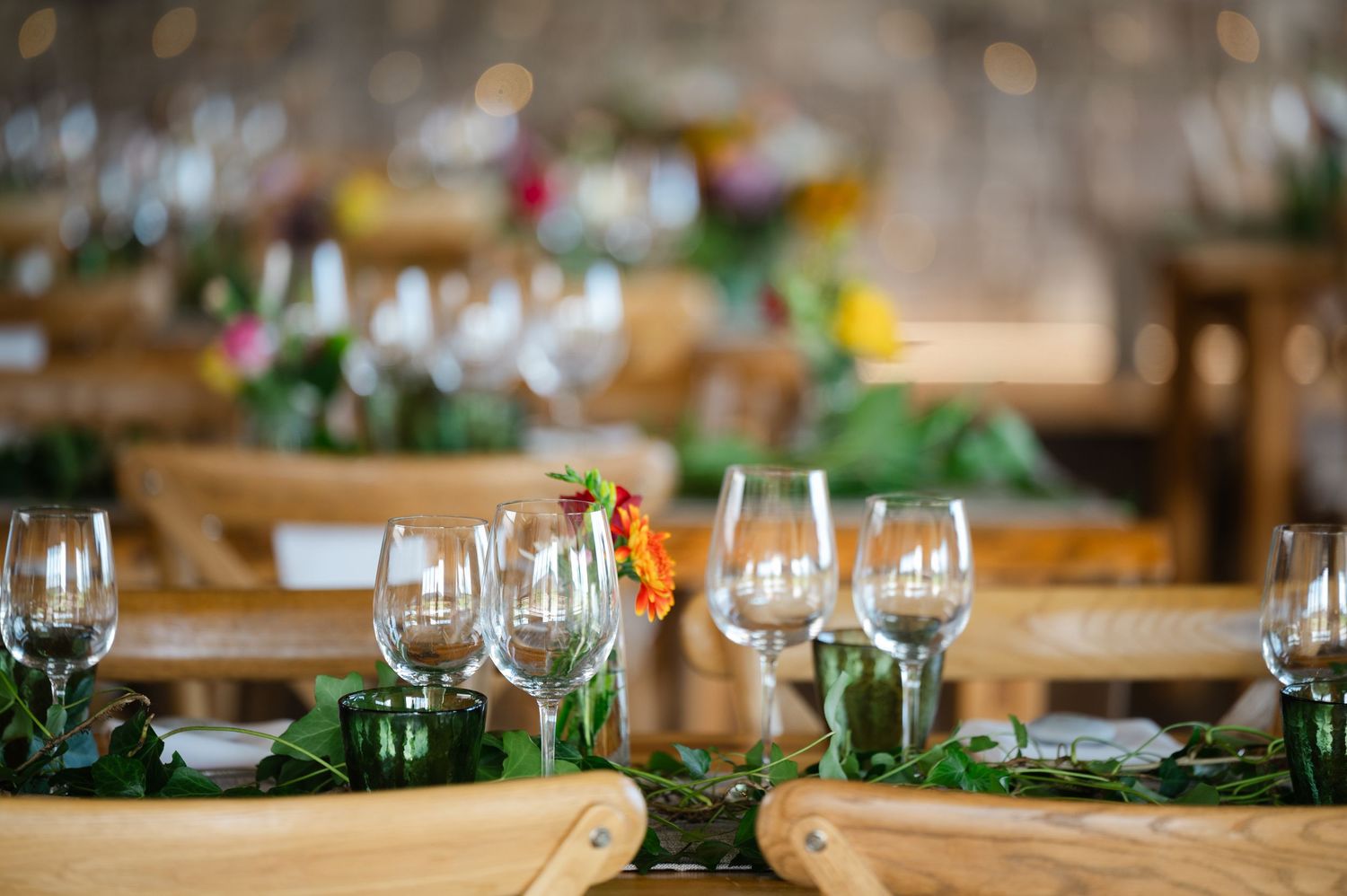 Reception tables in a rustic venue, decorated with greenery, glassware, and floral centrepieces