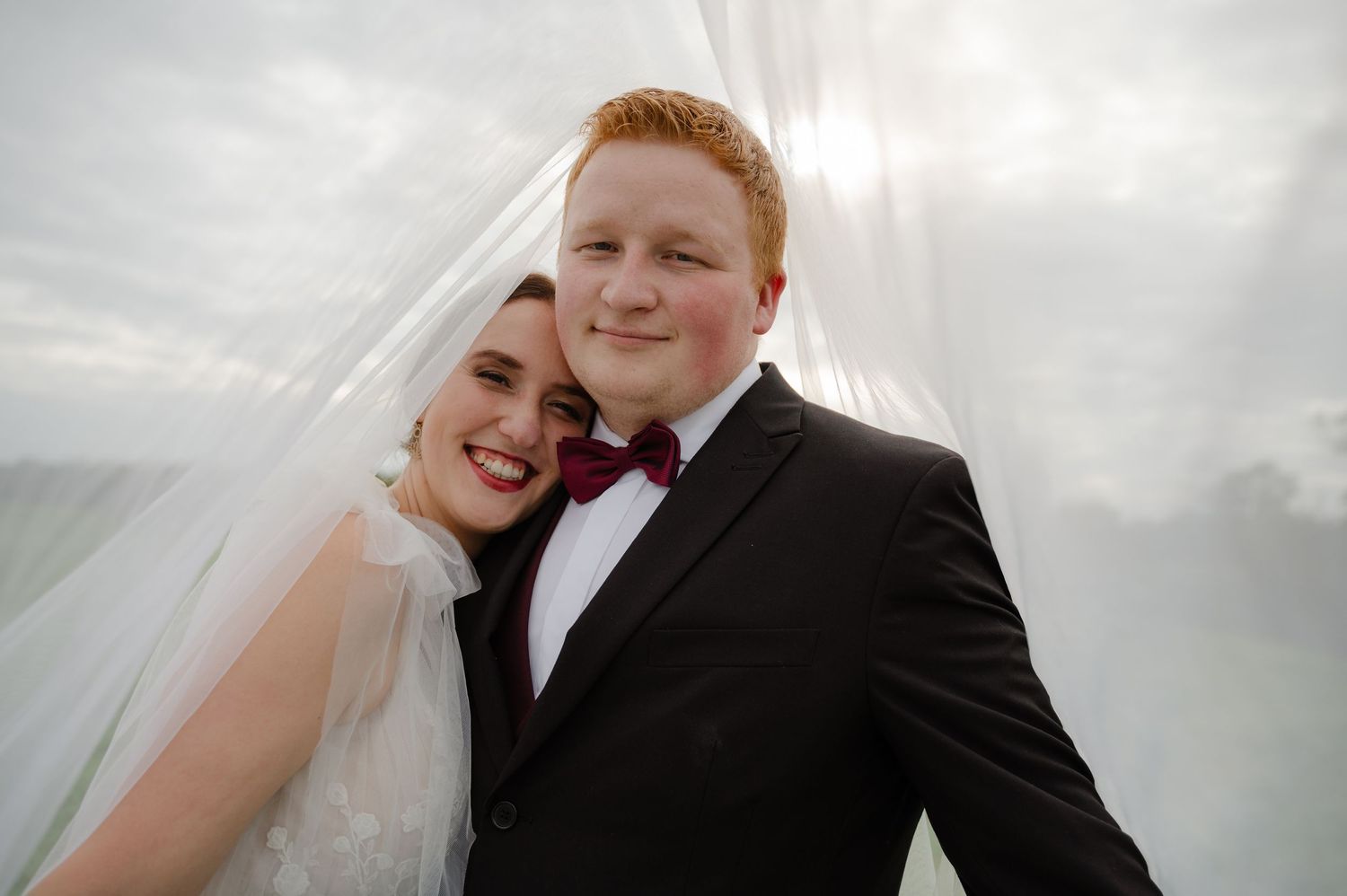 Bride and groom smiling under a flowing veil on their wedding day