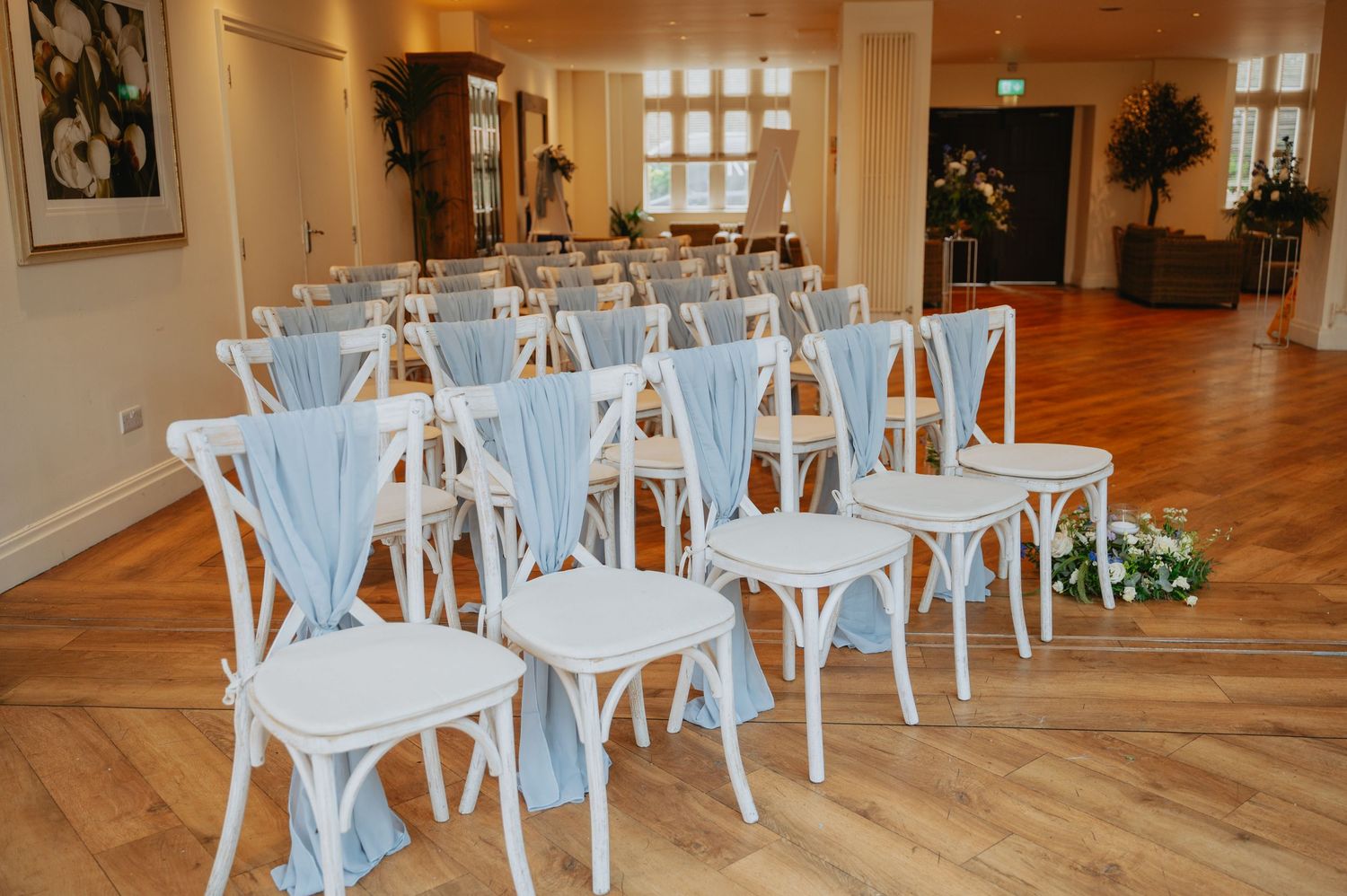 Wedding reception setup with white chairs tied with ribbon and elegantly decorated round tables, ready for guests in a charming venue.
